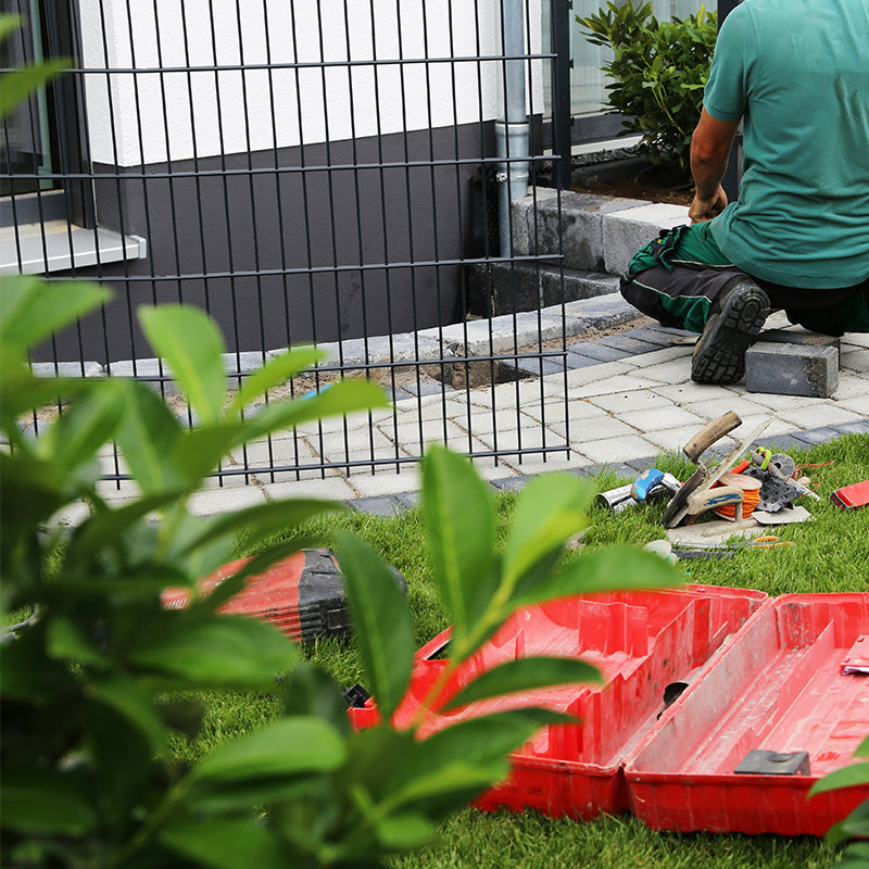 Person in grünem Shirt und Arbeitshose beim Gartenbau.